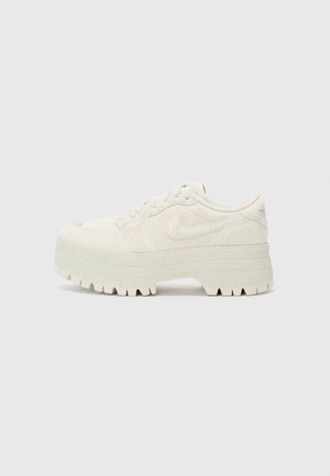 Baltas teksturēts čības ar biezām, blokveida zolem, kas dekorēta ar režģa rakstu. Šņorēšanas auklas un Nike logo uzspiedums sānos. Apaļš purngals.