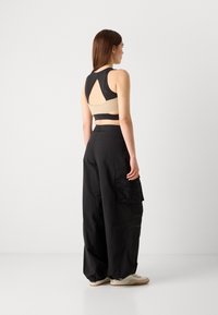 Canotta nera con design a taglio, abbinata a pantaloni cargo larghi con tasche. Il modello presenta una palette di colori neutri.