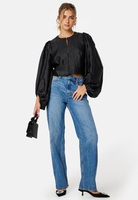 Zwarte cropped blouse met pofmouwen en een rits aan de voorkant. Gecombineerd met blauwe high-waisted straight-leg jeans en zwarte puntige hakken.