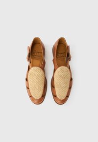 Καφέ δερμάτινα σανδάλια με πλεκτό ύφασμα στο πάνω μέρος των δαχτύλων, ανοιχτό σχέδιο και κλείσιμο με αγκράφα στο πλάι. Πάτος με επίπεδη σόλα και ανοίγματα. Υφή με ανάγλυφες λεπτομέρειες.