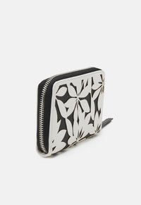 Portefeuille zippé avec une base noire et un design floral découpé en blanc. Texture lisse avec un détail de fermeture éclair contrastant. Forme carrée.