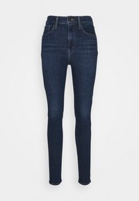 Jeans skinny de color azul oscuro, hechos de mezclilla, con una cintura alta, cinco bolsillos, costura dorada y una textura suave.