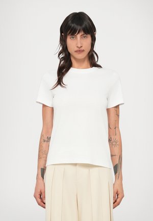 Fehér pamut póló kerek nyakkal, rövid ujjal és laza szabással. Egyszerű, mintázat vagy díszítés nélküli kialakítás.