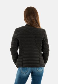 Zwarte, gewatteerde jas met verticale en chevronstiksels, voorzien van een staande kraag en een getailleerd ontwerp, gecombineerd met blauwe spijkerbroek.