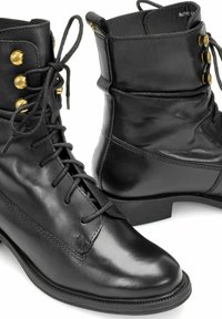 Czarne skórzane botki z wiązaniem na kostkę, z okrągłymi noskami, niskim obcasem i złotymi oczkami, pokazane z boku oraz z przodu.