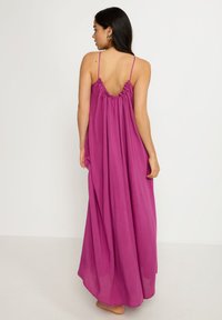 Largo vestido rosa con un corte relajado, que presenta tirantes finos y un escote trasero con volantes. Tejido suave con una silueta fluida.