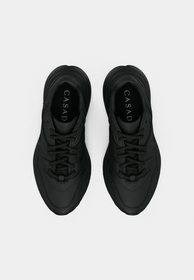 Μαύρα αθλητικά παπούτσια με λείο συνθετικό υλικό, στρογγυλεμένο σχήμα και υφασμένο πέλμα. Διαθέτουν κορδόνια και λογότυπο στα εσωτερικά πέλματα.