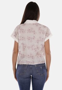 Blusa a maniche corte in tessuto leggero con motivo floreale in rosa chiaro su sfondo bianco, con colletto bianco a contrasto.
