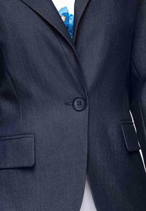 Veste blazer bleu marine foncé à un bouton avec revers crantés et poches à rabat, portée sur une chemise blanche avec un détail floral bleu.