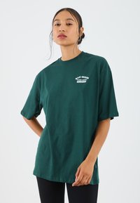 Dark green cotton t-shirt with short sleeves and a round neckline. Features white text logo "BAD SEEDS PLANT STORE" on the chest.