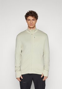 Light beige zip-up jacket made from soft material, featuring a high collar, long sleeves with thumbholes, and a sleek, minimalist design.