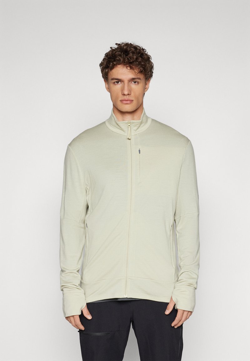 Giacca zip con cappuccio alta di colore beige chiaro, realizzata in materiale morbido, con maniche lunghe dotate di aperture per il pollice e un design elegante e minimalista.