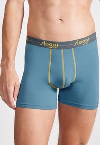 Boxers cortos de algodón azul con costuras amarillas y una cinturilla elástica gris que presenta el logo "sloggi".