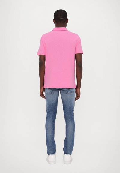 Polo rose à manches courtes, en tissu coton ; jeans en denim bleu ; baskets blanches. Vue de derrière. Design simple, sans motifs visibles.