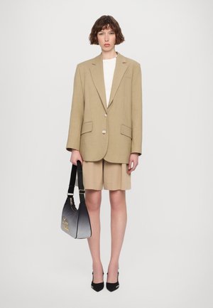 Blazer en lin beige avec deux boutons, accompagné de shorts beiges. Sac à main noir avec des détails en dégradé et un logo, et escarpins noirs à bout pointu.