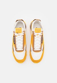 Reebok-sneakers med ett vitt och gult färgschema, med bruna accenter, textilmaterial och platta snören, designade för komfort och stil.