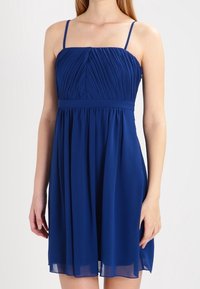 Modrá bezrukávová šaty s plisovaným korzetem, přiléhavým pasem a splývavou sukní. Vyrobeno z lehké tkaniny, má tenké ramínka a kulatý výstřih.
