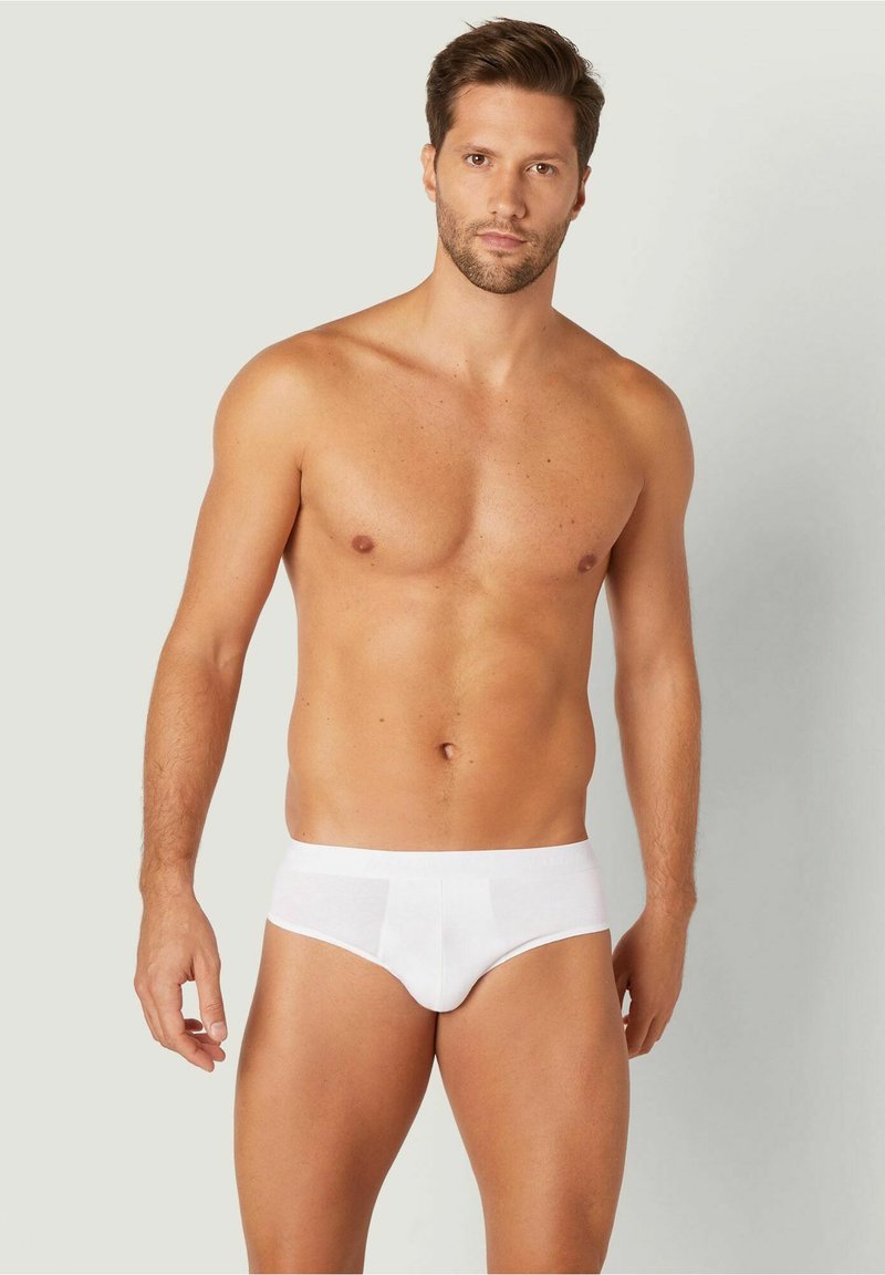 Weiße Baumwollslips mit nahtlosem Design, elastischem Bund und enganliegendem Schnitt, präsentiert von einem Modell vor einem neutralen Hintergrund.
