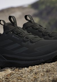 Scarpe da trail running nere Adidas Gore-Tex con suole strutturate posizionate su un terreno roccioso all'aperto.
