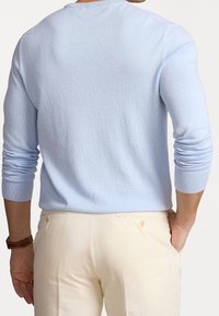 Jasnoniebieski sweter dzianinowy z długimi rękawami, okrągłym dekoltem i ściśniętymi mankietami, w połączeniu z beżowymi spodniami z tylnymi kieszeniami i detalem w postaci guzika.