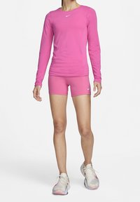 Top atletico a maniche lunghe fucsia aderente abbinato a pantaloni corti coordinati. Presenta il logo Nike, una texture liscia e un materiale elastico progettato per le prestazioni.
