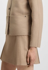 Beige wool-blend jacket with a tailored fit and front buttons, paired with a beige pinstriped skirt. Both pieces feature soft textures.