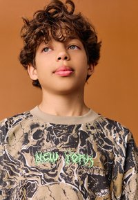 Hanorac cu mâneci lungi, cu imprimeu grafic, cu un design întunecat cu cranii și text verde "NEW YORK", confecționat din țesătură moale de bumbac.