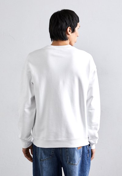 Hvit genser med lange ermer, ribbestrikkede mansjetter og krage, vist fra baksiden. Kombinert med blå denimjeans. Glatt tekstur.