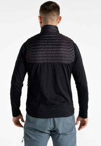 Schwarze Jacke mit gepolstertem oberen Rücken und langen Ärmeln, die eine glatte Textur und ein eng anliegendes Design aufweist. Sichtbare Reißverschlusstaschen.