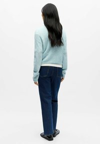 Lys blå cropped genser med lange ermer, kombinert med m�ørkeblå jeans med rette ben og svarte sko, sett bakfra.