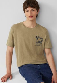 Olijfgroen t-shirt met korte mouwen en een ronde hals, met een blauwe afbeelding van palmbomen en tekst op de linkerkant van de borst.