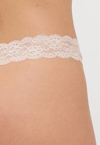 Kantafwerking in zachtroze, met bloemenpatronen en golvende randen, bevestigd aan een naadloze band voor comfortabel draagcomfort.