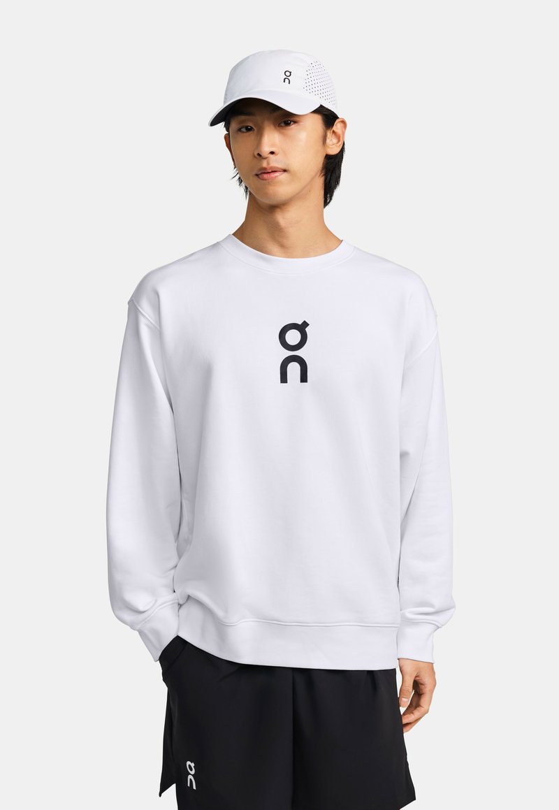 Sweatshirt blanc avec un logo noir sur le devant, associé à un short noir. Comprend également une casquette blanche avec des accents ventilés.