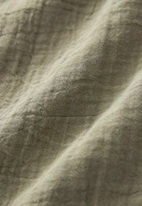 Tissu vert clair texturé avec une surface froissée, fabriqué à partir d'un matériau naturel, présentant des variations subtiles de couleur et de motif.
