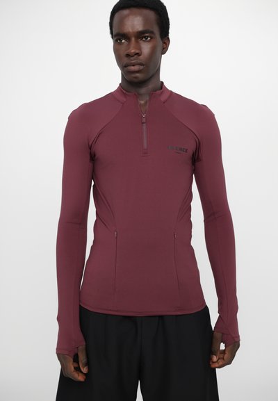 Burgundy long-sleeve athletic top features a half-zip neckline and flat seams, made from stretchy material with thumbholes on sleeves.