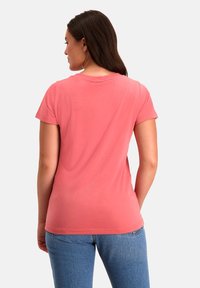 Koraalroze T-shirt met korte mouwen en ronde hals, gemaakt van zachte katoen, gedragen met blauwe spijkerbroek.