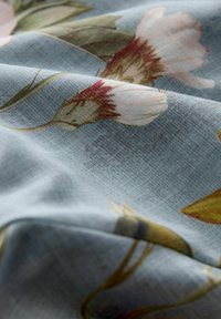 Floraler Stoff mit hellblauem Hintergrund, der detaillierte Illustrationen von Blumen in sanften Rosa-, Creme- und Grüntönen sowie eine glatte Textur zeigt.