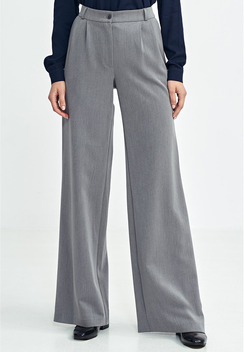 Szare spodnie o szerokich nogawkach wykonane z teksturowanej tkaniny, z przednimi zakładkami, zapięciem na guzik i wysokim stanem, zestawione z czarnymi butami.