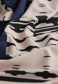 Tissu crème avec des motifs de vagues abstraites noires, présentant une texture lisse et un drapé doux, mettant en valeur un mélange d'accents bleu foncé.