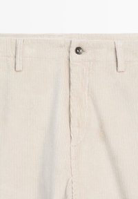 Pantalons en velours côtelé beige clair avec des rainures verticales, dotés d'une fermeture à bouton et de poches avant plates. Texture douce, léger brillant.
