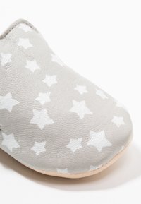 Zapato de cuero gris con puntera redondeada, que presenta un patrón de estrellas blancas. La textura parece suave con un acabado natural.