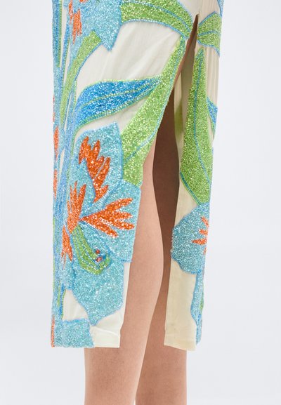 Μοτίβο με χάντρες σε σχέδιο λουλουδιών σε μπλε, πράσινο και πορτοκαλί σε εκρού ύφασμα με πολύ ψηλή σκίσιμο που αποκαλύπτει γυμνό δέρμα από κάτω.