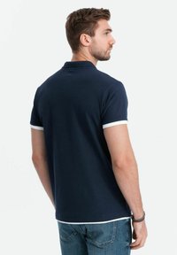 Marinblå pikétröja med korta ärmar, med vit kant vid ärmsluten och kragen, designad i en klassisk passform, tillverkad av mjukt tyg.