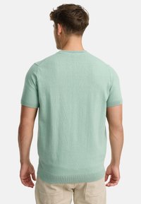 Myntgrøn kortærmet strikket sweater, rund halsudskæring, ribbede manchetter og kant, struktureret stof, slank pasform, båret med beige bukser.