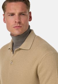 Beige strukturerad stickad polo med krage och en kontrasterande grå polo under, med en knappdetalj.