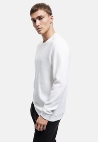 Felpa bianca testurizzata con scollo rotondo e maniche lunghe, caratterizzata da un sottile motivo a coste e dettagli sulle cuciture laterali.