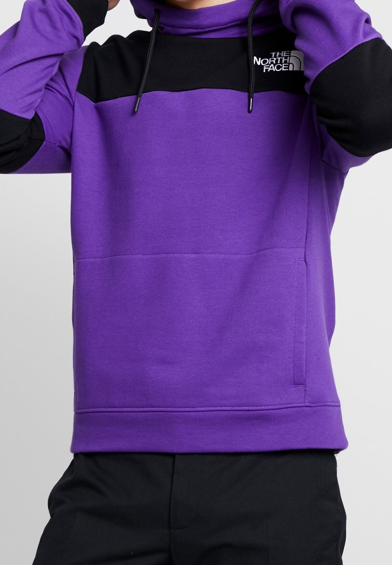 Lila sweatshirt med svarta accenter, som har huva, framficka och broderad logotyp. Slät textur med ribbade muddar. Justerbara snoddar.