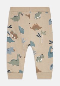 Pantaloni beige per bambini con vita elastica, decorati con giocosi dinosauri e piccole palme in tonalità di verde, blu e marrone tenui.