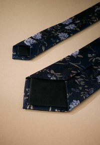 Cravate florale en tissu de soie bleu marine foncé ornée de motifs floraux dorés et argentés ; extrémités effilées avec une doublure noire lisse.