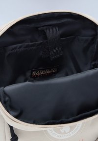 Cream-colored bag interior with black lining. Features a label, straps, and a smooth texture. Zipper closure at the top.